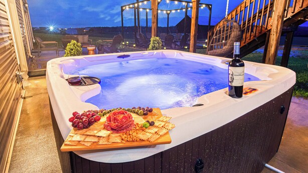 Ein Whirlpool mit Holzterrasse, umgeben von Stühlen und einem Tisch mit Weinflasche und Snacks.