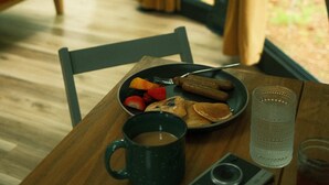 A dining table with a plate of food, a mug, a camera, and a glass of water. - 22-ft dome w/ stargazing loft and full bath - 08 (Freeport)