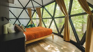 Ein Zimmer mit Bett, einem Sessel und großen Fenstern mit Vorhängen.