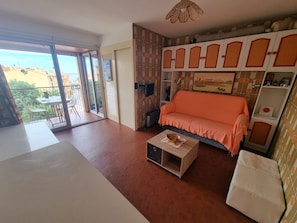 A living room with a sofa, a coffee table, and a balcony with outdoor furniture.