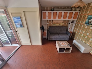 Uma sala de estar com um sofá cinza, uma mesinha com toalha xadrez, parede estampada e uma porta de vidro deslizante que dá para área externa.