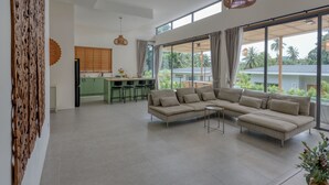 A spacious living area with a large L-shaped sofa, a dining table with chairs, and a kitchen in the background. - Tropical Poolside Retreat by Sea N' Rent (Ko Pha-ngan)