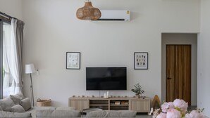 A modern living room with a large grey sofa, a flat-screen TV, a wicker pendant light, and a wooden door. - Tropical Poolside Retreat by Sea N' Rent (Ko Pha-ngan)