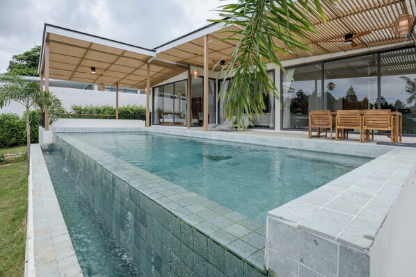 A modern house with a swimming pool, wooden deck, and glass doors leading to a covered outdoor area.