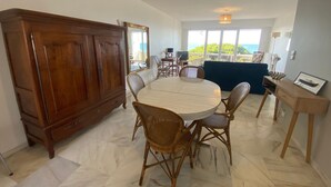 Un coin repas avec une table ronde, des chaises en osier, un buffet en bois et une vue sur l’extérieur.