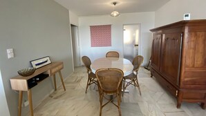 Un coin repas comprenant une table ronde, quatre chaises en osier, un buffet en bois et une décoration murale à motifs.