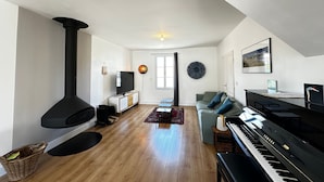 A spacious living room with a black piano, a television, a fireplace, and a large window. - Spacious 4-Bedroom House, Central Fouras, Near Beaches (Fouras)