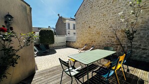 A courtyard with a wooden deck, a table with chairs, and a stone wall. - Spacious 4-Bedroom House, Central Fouras, Near Beaches (Fouras)