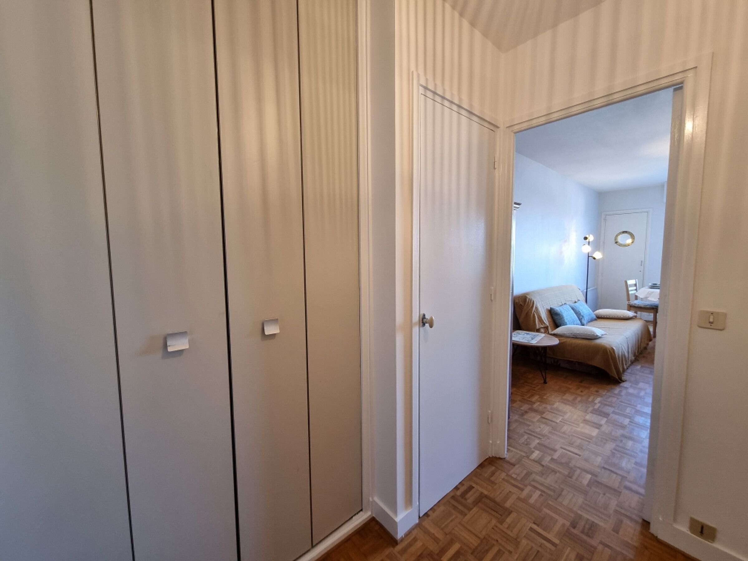 A room with a bed, bedside table, and a mirror. There is a door leading to another room.