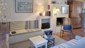 A living room with a sofa, a television, a fireplace, and a bookshelf. - Charming fisherman's house, 4 pers, near beach, Saint-Gildas-de-Rhuys, wifi (Saint-Gildas-de-Rhuys)