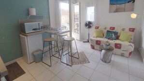 A compact living space with a kitchenette, a dining area, a sofa with cushions, and a fan. - T2 Saint-Pierre-La-Mer - Parking - 3/4 people (Fleury-Saint-Pierre-la-Mer)