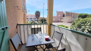 A small outdoor table with chairs, a glass, and a red cup on a balcony with a view of buildings and a palm tree. - T2 Saint-Pierre-La-Mer - Parking - 3/4 people (Fleury-Saint-Pierre-la-Mer)