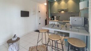 A compact kitchen with a white countertop, three stools, a microwave, and a TV mounted on the wall. - T2 Saint-Pierre-La-Mer - Parking - 3/4 people (Fleury-Saint-Pierre-la-Mer)