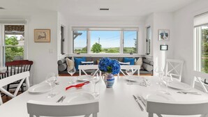A dining area with a white table set for four, a vase of blue flowers, and a red lobster decoration. - Private Beach, Water Views, Incredible Location! (Chatham)