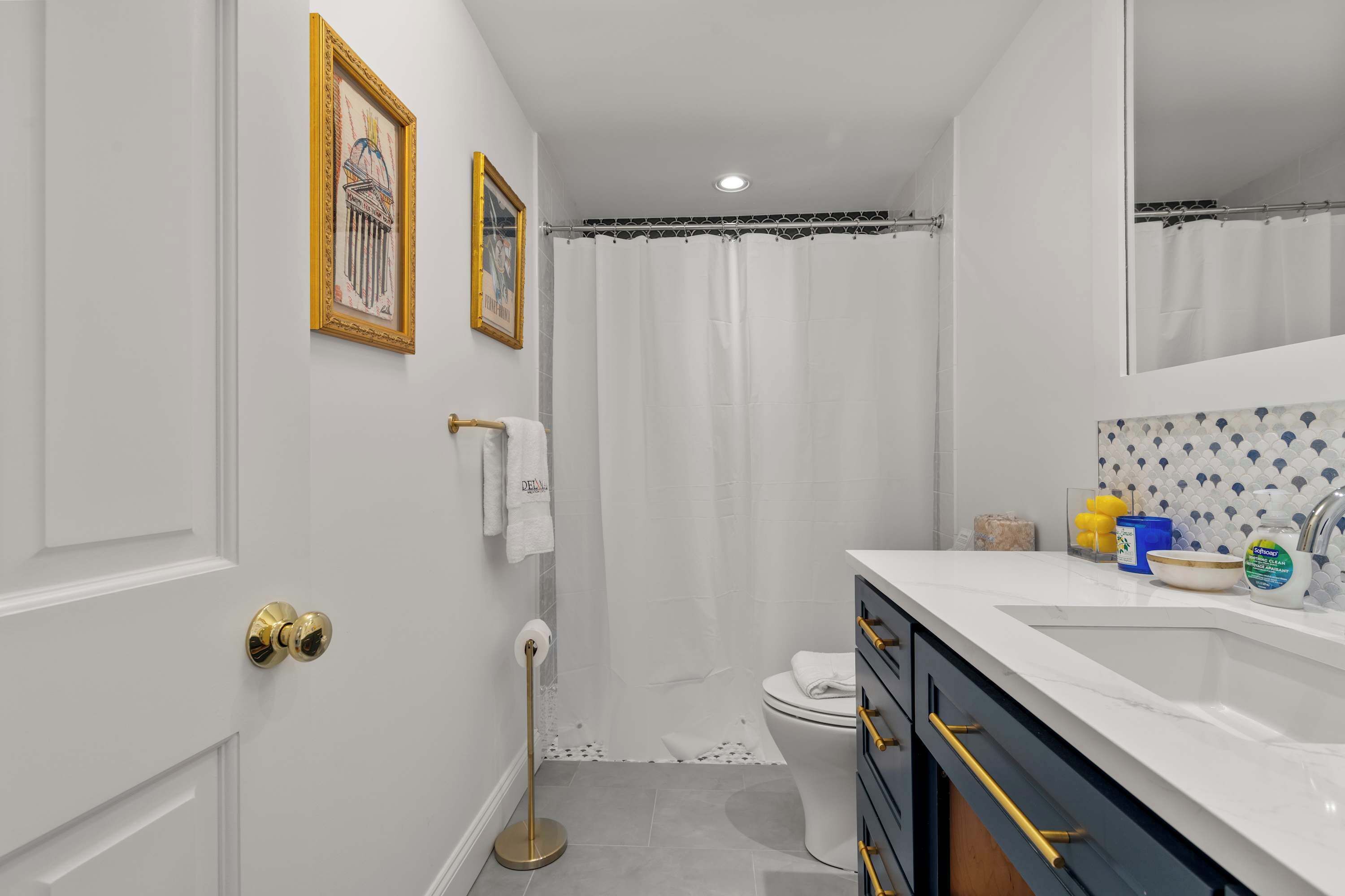 Une salle de bain avec un lavabo blanc, des robinetteries dorées, des toilettes et un rideau de douche.