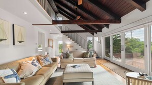 A spacious living area with a high ceiling, a staircase, and large windows providing a view of the outdoors. - Private Beach, Water Views, Incredible Location! (Chatham)