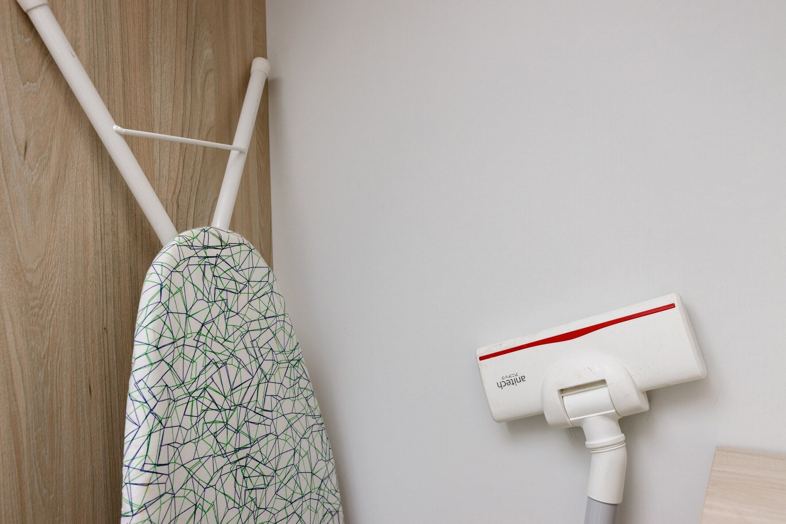 A wall-mounted vacuum cleaner, a patterned garment hanging on a rack, and a wooden surface.