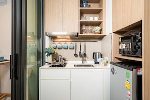 Una kitchenette compacta con microondas, hervidor y lavamanos pequeño.