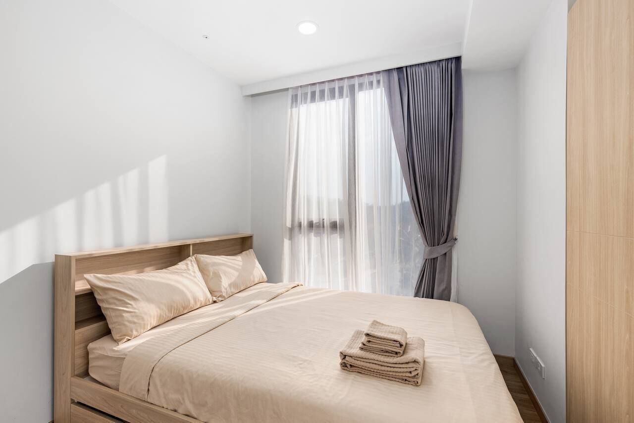 A minimalist bedroom with a wooden bed frame, a neutral-colored bedspread, and a neatly folded set of towels on the bed.