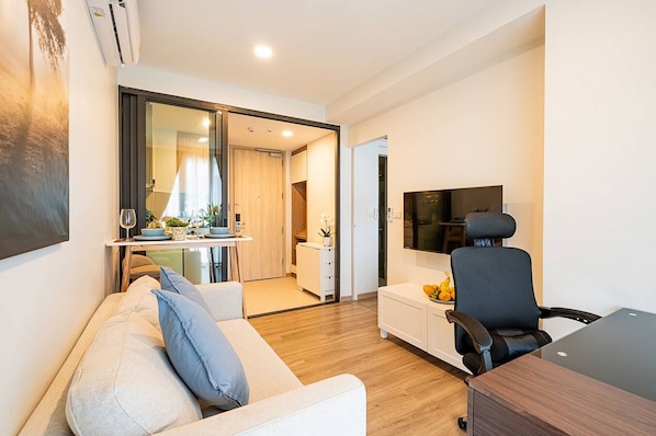 A modern living room with a sofa, a dining area with a table and chairs, a TV mounted on the wall, and a small cabinet.