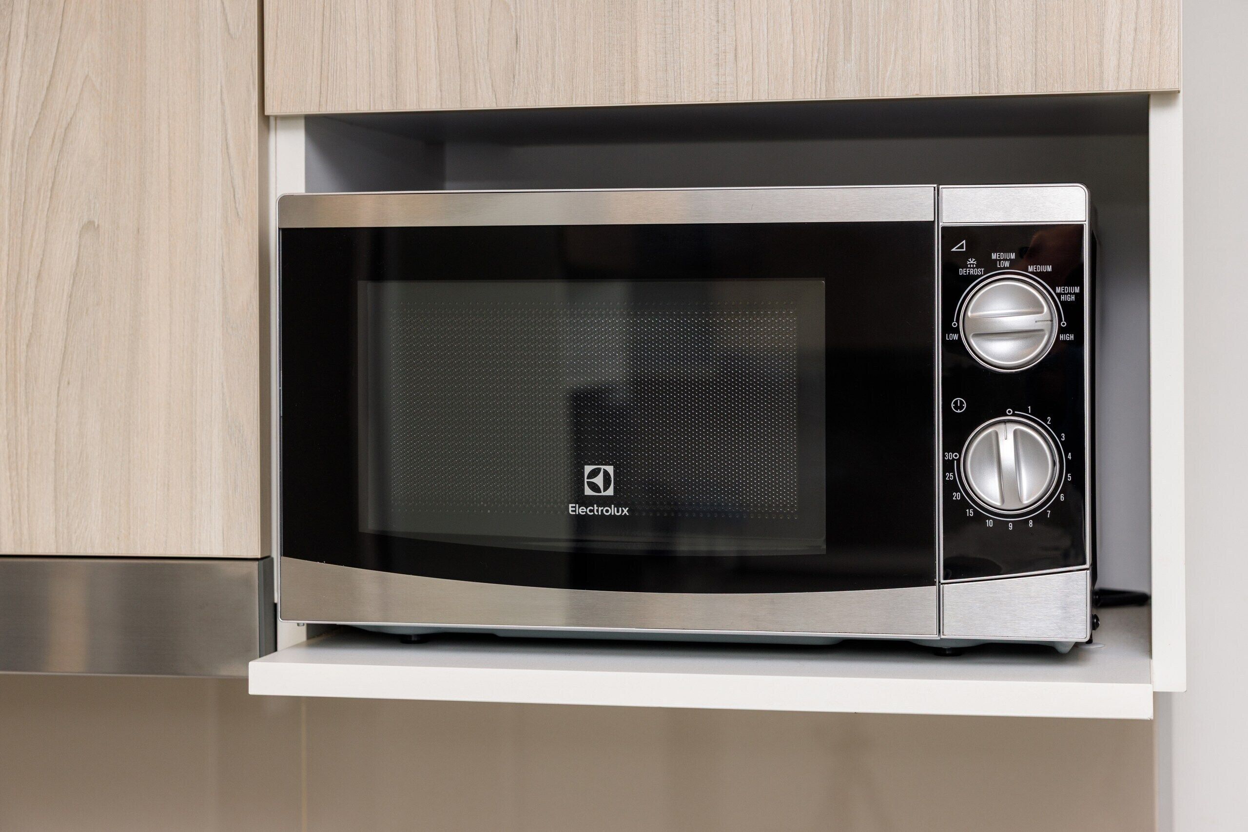 A modern Electrolux microwave oven with a digital display and control knobs, housed in a kitchen with light wood cabinetry.