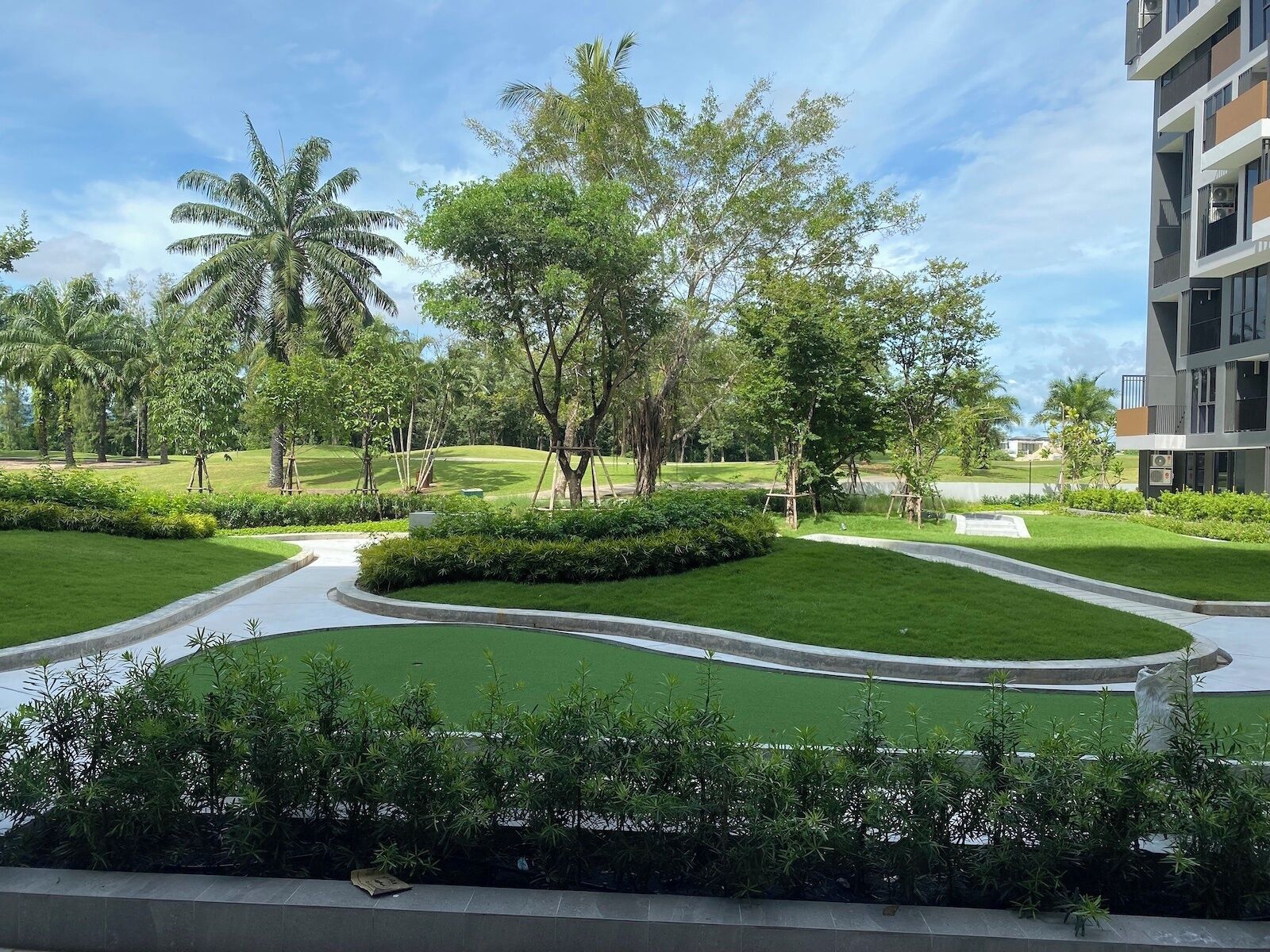 Un giardino curato con palme, un percorso sinuoso e un edificio moderno con balconi.