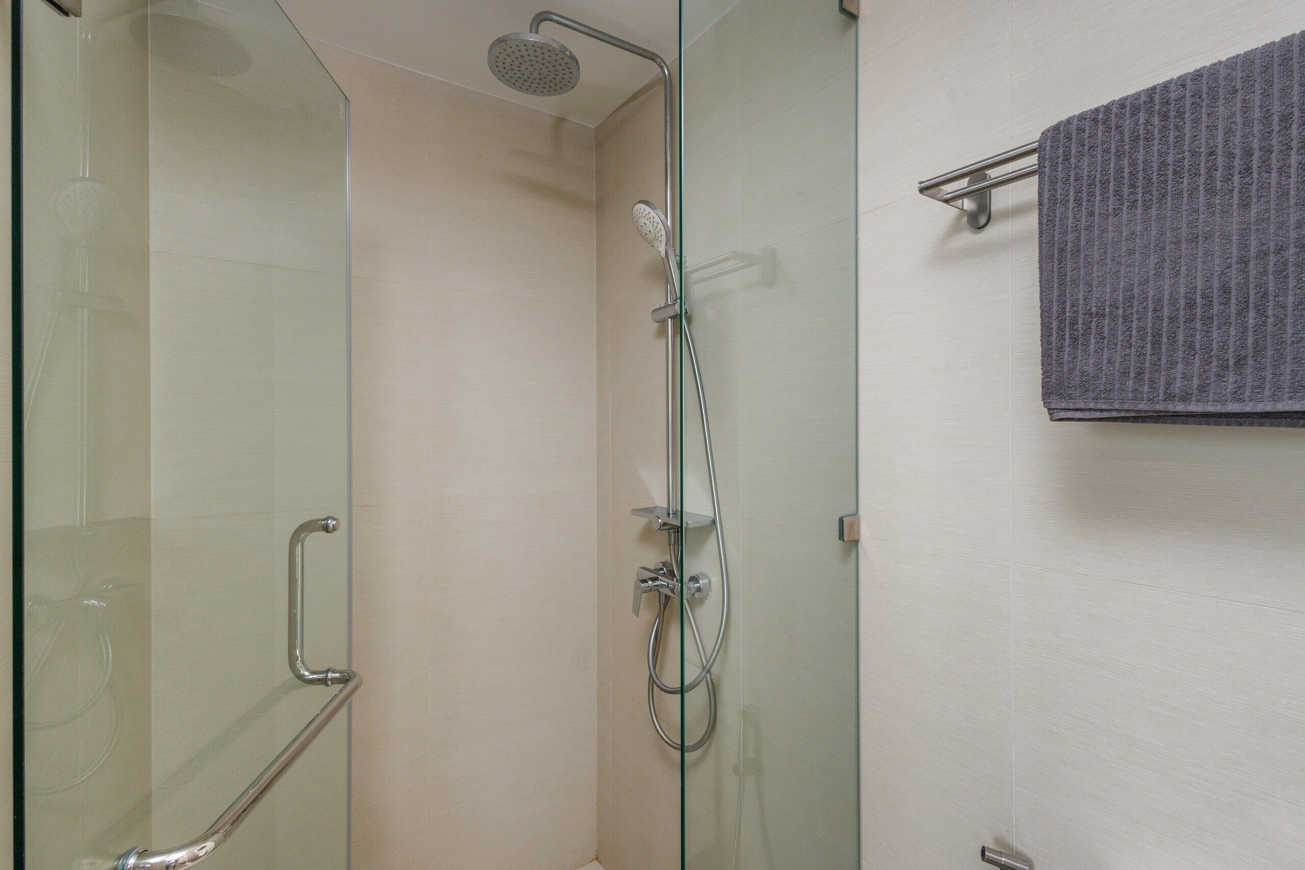 Une douche fermée par des parois en verre, dotée d’un pommeau de douche à main et d’une barre pour suspendre une serviette pliée.