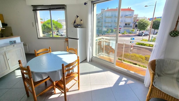 Un comedor con una mesa redonda y sillas, un refrigerador, una ventana con vistas a edificios y una calle, y un ventilador de techo.