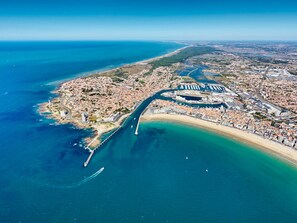Luftaufnahme einer Küstenstadt mit einer markanten, gebogenen Straße, einem Yachthafen und einem Strand.