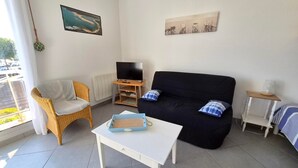 Sala de estar con sofá, televisor, sillón de mimbre, una mesita y ventana con vistas al exterior.