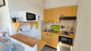 Cocina compacta con gabinetes de madera, microondas, fregadero y estufa.
