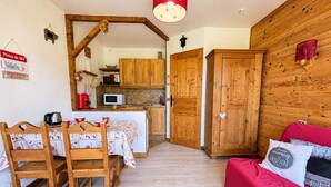 A cozy room with a wooden dining table, chairs, a red sofa, and a kitchen area with wooden cabinets and a microwave. - Cozy ski-in studio with parking, pets allowed (Notre-Dame-de-Bellecombe)