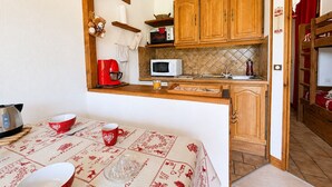 A compact kitchen with wooden cabinets, a microwave, a coffee maker, and a table with a red tablecloth. - Cozy ski-in studio with parking, pets allowed (Notre-Dame-de-Bellecombe)