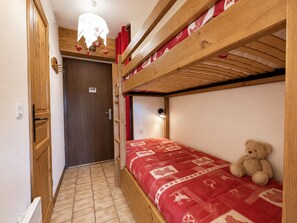 Une chambre avec un lit superposé, un ours en peluche sur le lit du bas, une porte et un luminaire au plafond.