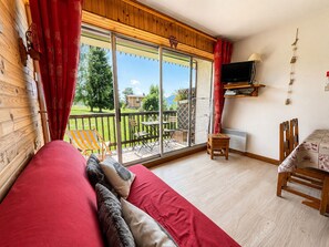 A cozy room with a red sofa, a small table, and a TV mounted on the wall. - Cozy ski-in studio with parking, pets allowed (Notre-Dame-de-Bellecombe)
