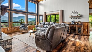 Un salon spacieux avec un grand canapé d’angle, une cheminée et une vue sur les montagnes grâce à de grandes fenêtres.