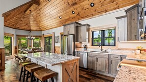 Une cuisine spacieuse dotée d’un grand îlot central, d’un plafond en bois et de grandes fenêtres.
