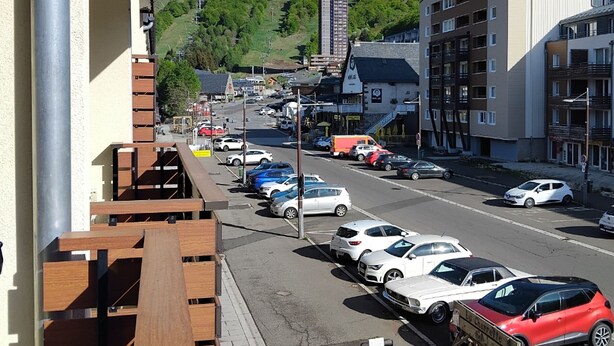 Vista da rua com carros estacionados, edifícios e uma colina ao fundo.