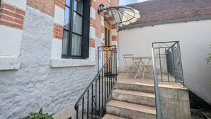 A staircase leading to a covered outdoor area with a table and chairs, a window with black shutters, and a brick wall. - Rural charm and relaxation near Loire castles (Chabris)