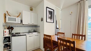 Eine kompakte Küche mit weißen Schränken, einer Mikrowelle und einem Spülbecken. Es gibt einen Essbereich mit einem Holztisch und Stühlen.