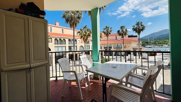 Ein Balkon mit Tisch und Stühlen, der auf einen Yachthafen mit Booten und Palmen blickt.