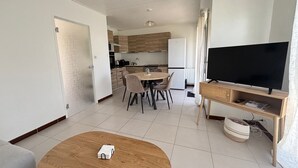 A modern living room with a wooden coffee table, a flat-screen TV on a wooden stand, and a dining area with a round table and chairs. - House in Les Sables-d'Olonne with garden, 4 sleeps (Les Sables-d'Olonne)
