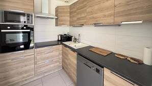 A modern kitchen with wooden cabinets, a black countertop, a dishwasher, a microwave, and a stove. - House in Les Sables-d'Olonne with garden, 4 sleeps (Les Sables-d'Olonne)