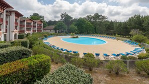 Un área de piscina con sillones reclinables azules, un edificio con balcones y vegetación circundante.
