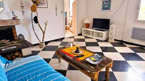 A living room with a checkered floor, a sofa, a coffee table with magazines, a TV, and a fireplace. - Charming T3 for 6 pers. with parking in Banyuls-Sur-Mer (Banyuls-sur-Mer)