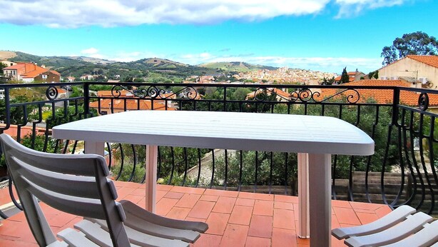 A balcony with a table and chairs, offering a view of a town and hills. - Charming T3 for 6 pers. with parking in Banyuls-Sur-Mer (Banyuls-sur-Mer)