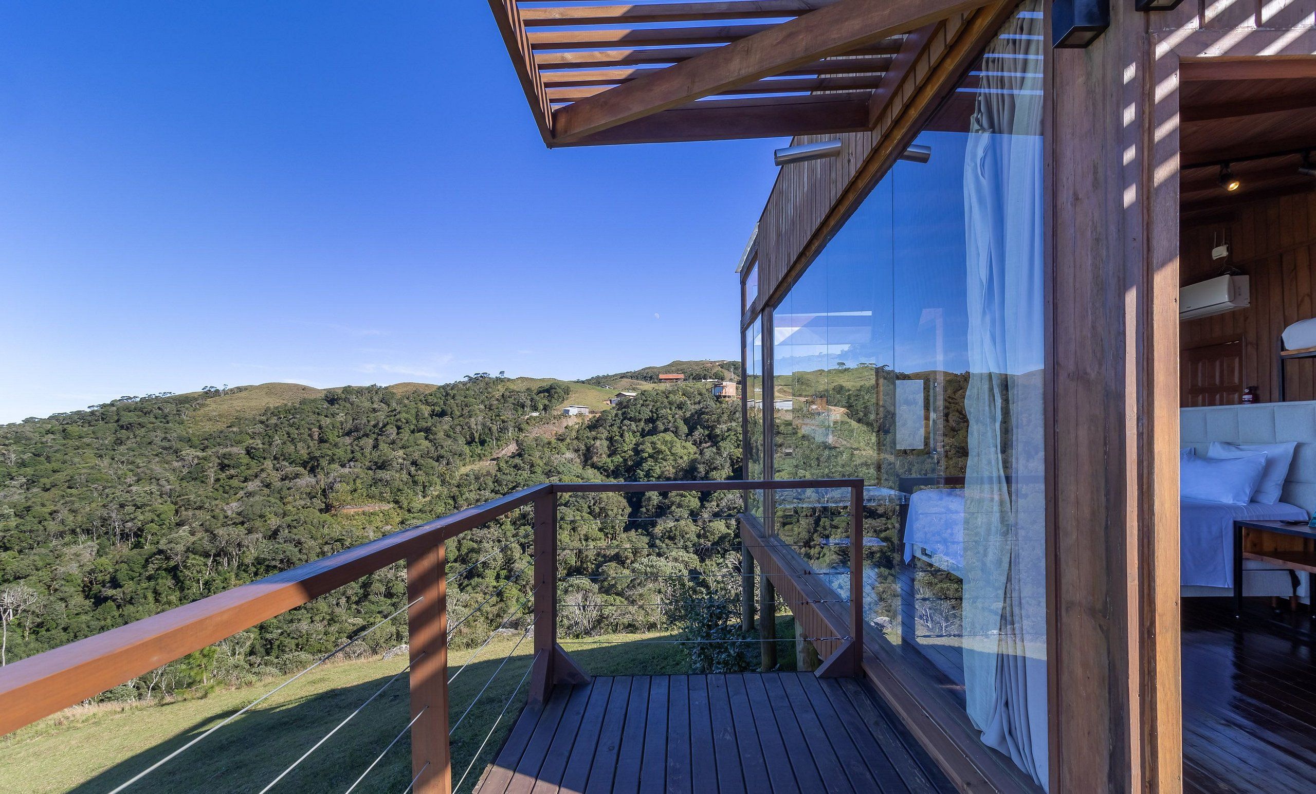 Una terraza de madera con barandilla de vidrio que da a un paisaje montañoso.