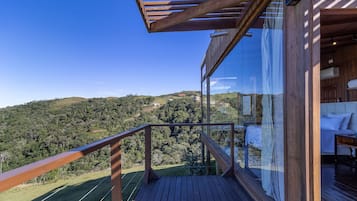 Una terraza de madera con barandilla de vidrio que da a un paisaje montañoso.