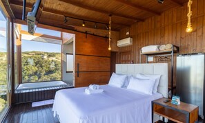 Un dormitorio con una cama grande, vistas al exterior, techo de madera y un refrigerador moderno.