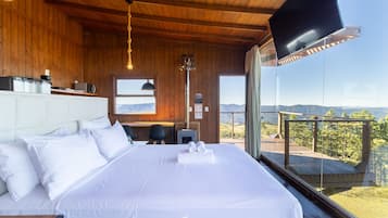 A bedroom with a large bed, wooden walls, a TV, and a balcony with a mountain view.